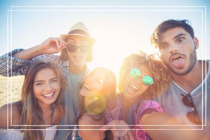 Group of friends having fun taking a selfie. They are all looking at the camera and smiling and laughing. Some are making funny faces. Sun with lens flare.