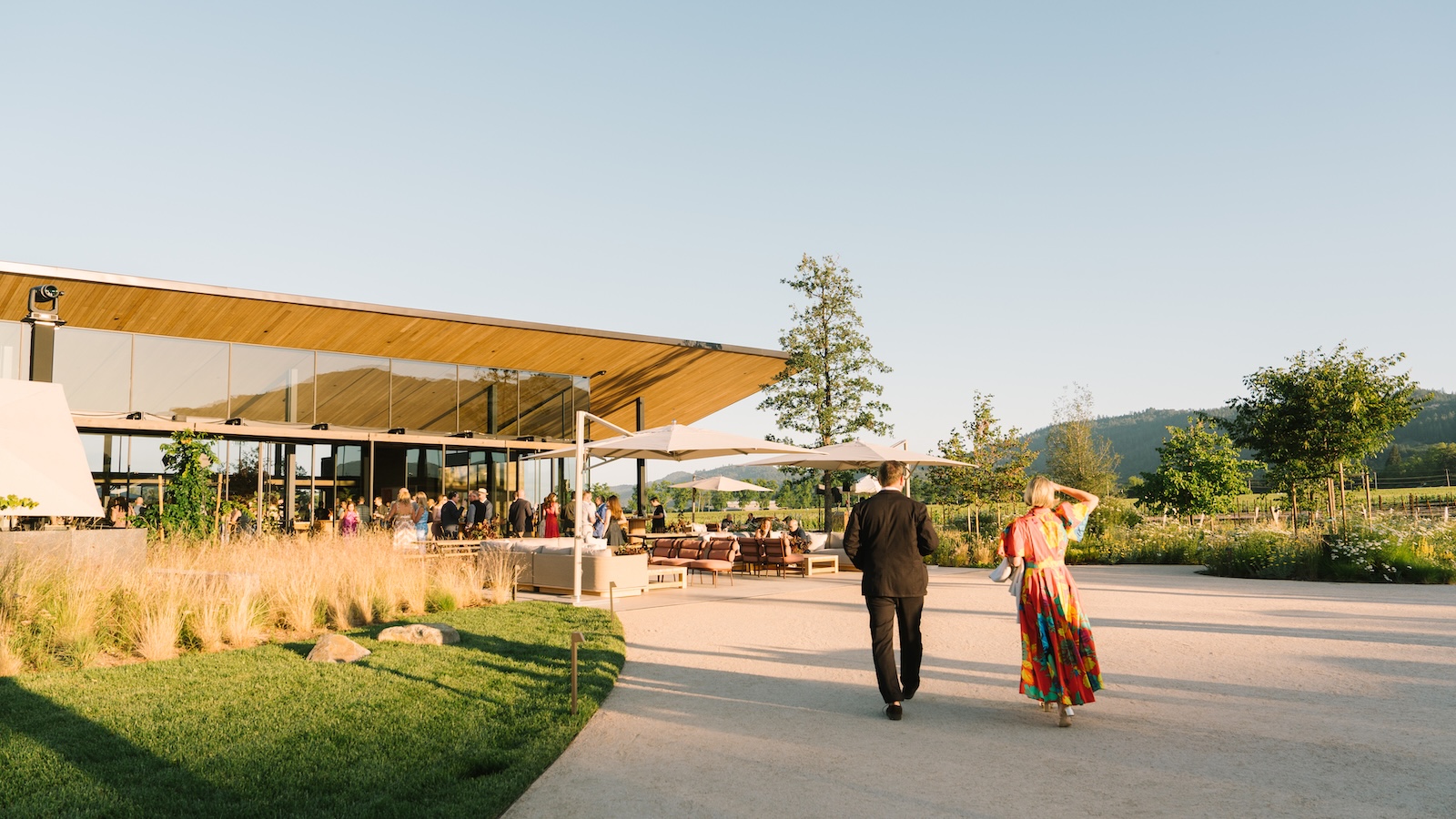 Guests walking towards the new hospitality wing at Robert Mondavi Winery, where a glass-walled room and outdoor terrace look out onto the vineyard.