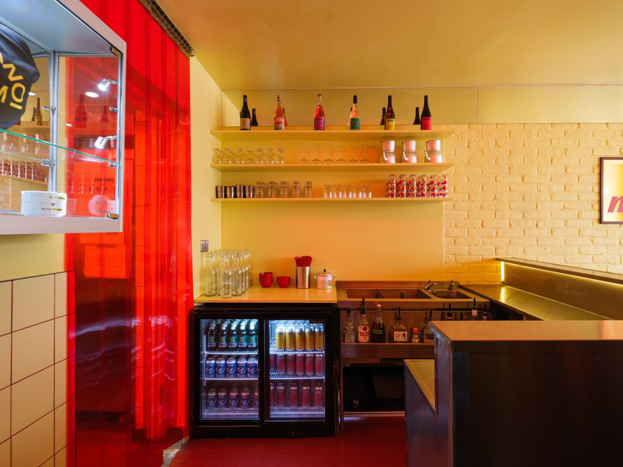 An inventively designed, small eatery features buttery brick walls, red floors and furniture mixed with chrome decor, and spherical, softly glowing opaque glass sconces.