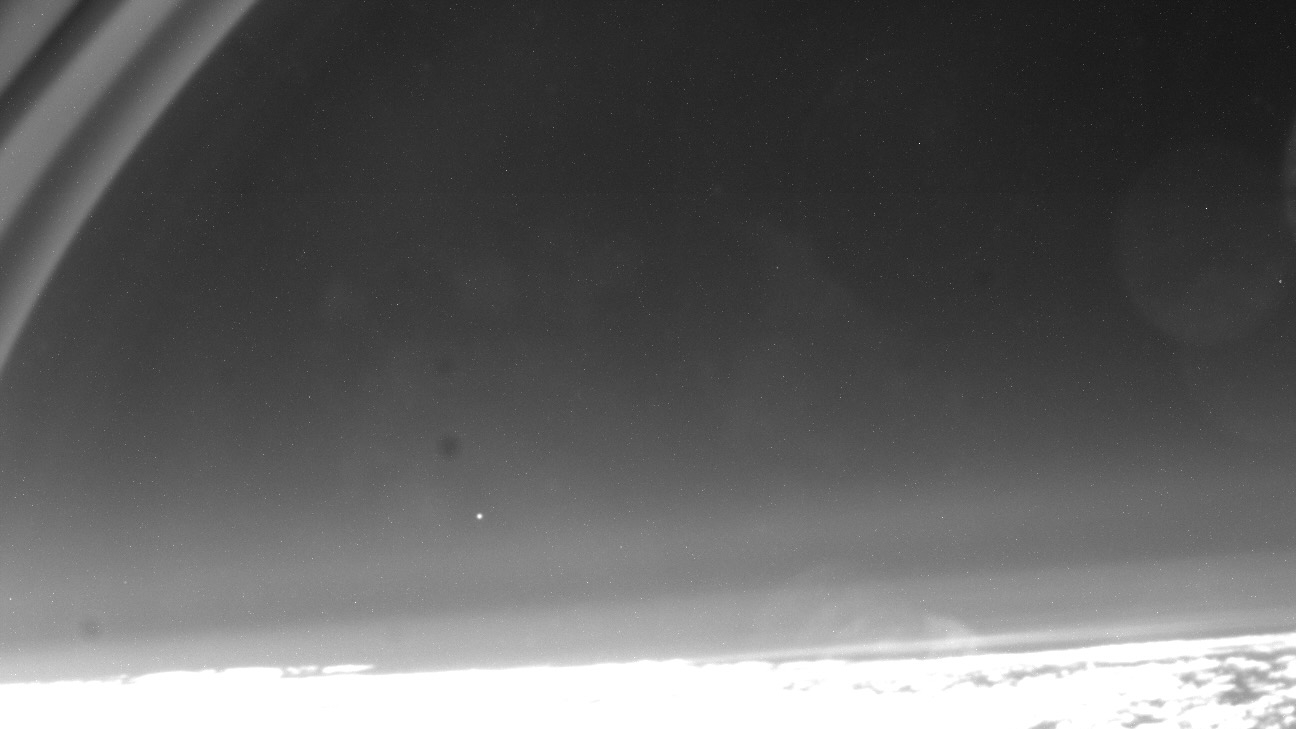 black and white photo of a satellite reentry to earth's atmosphere, showing the spacecraft as a distant white dot in the sky