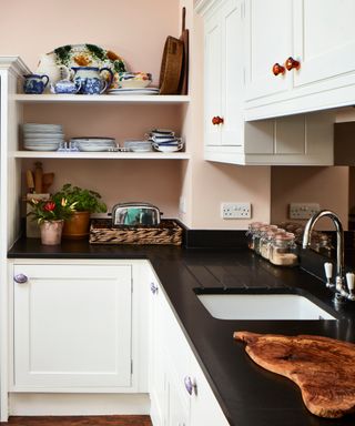 white kitchen cabinets with black worktops and pale pink walls