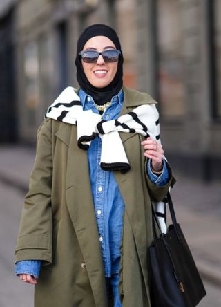 A woman dressed in multiple light layers, including a denim shirt, coat and headscarf