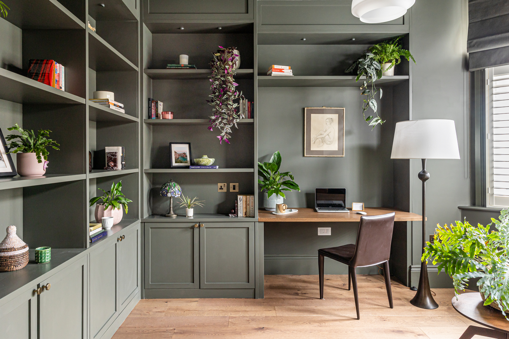 green color-drenched home office with built-ins and a timber floating desk with a floor lamp next to it and brown leather chair