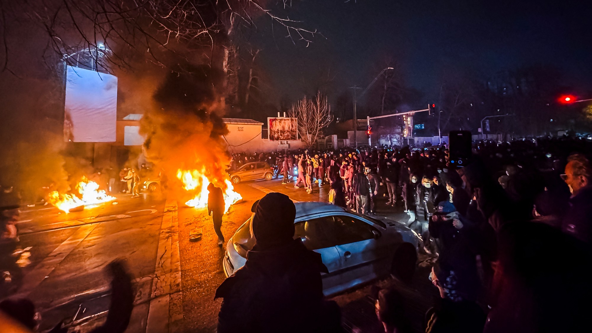 Iranian protesters look on as a fire burns in the street during a nighttime demonstration in Tehran
