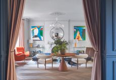 A living room with herringbone wood flooring, two boucle chairs and a ceiling rose