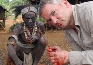 Papua New Guinea, Western Province: Piers Gibbon with song leader Tidikawa, who was responsible for identifying 'magic men' who would be killed and eaten. Gibbon is helping butcher a pig with the bamboo knife he holds. The same sort of knife was once used to butcher humans.