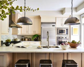 Modern kitchen with cream cabinetry, two round metal pendants, black stool seating