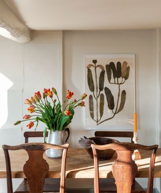 White painted dining room with wooden table and chairs and vase of orange tulips on tabletop
