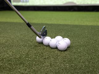 A group of six Titleist golf balls on a golf simulator mat in front of a screen