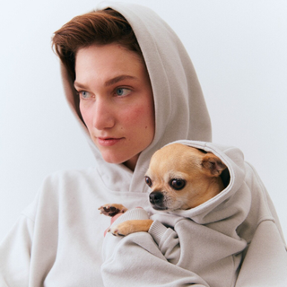 Woman holding dog who is wearing a matching beige hoodie