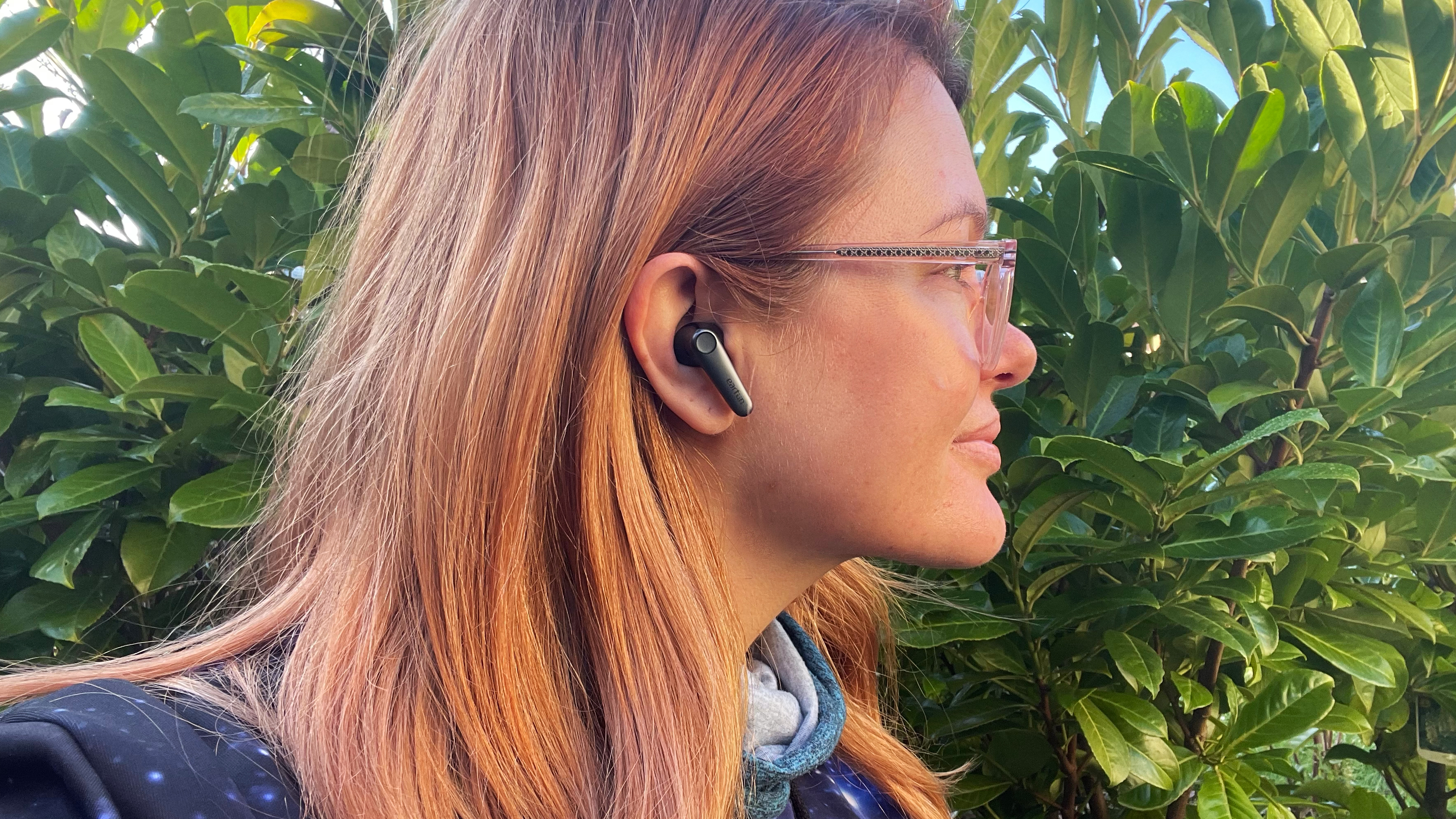 Earfun Air Pro 3 worn in the ears of a woman outdoors on wooden table