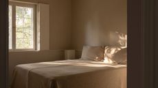Image of a minimalist, Scandi-style bedroom with a bed that has beige bedding and no headboard.