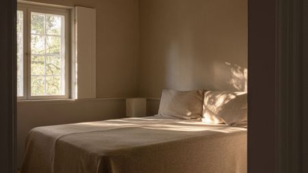 Image of a minimalist, Scandi-style bedroom with a bed that has beige bedding and no headboard.