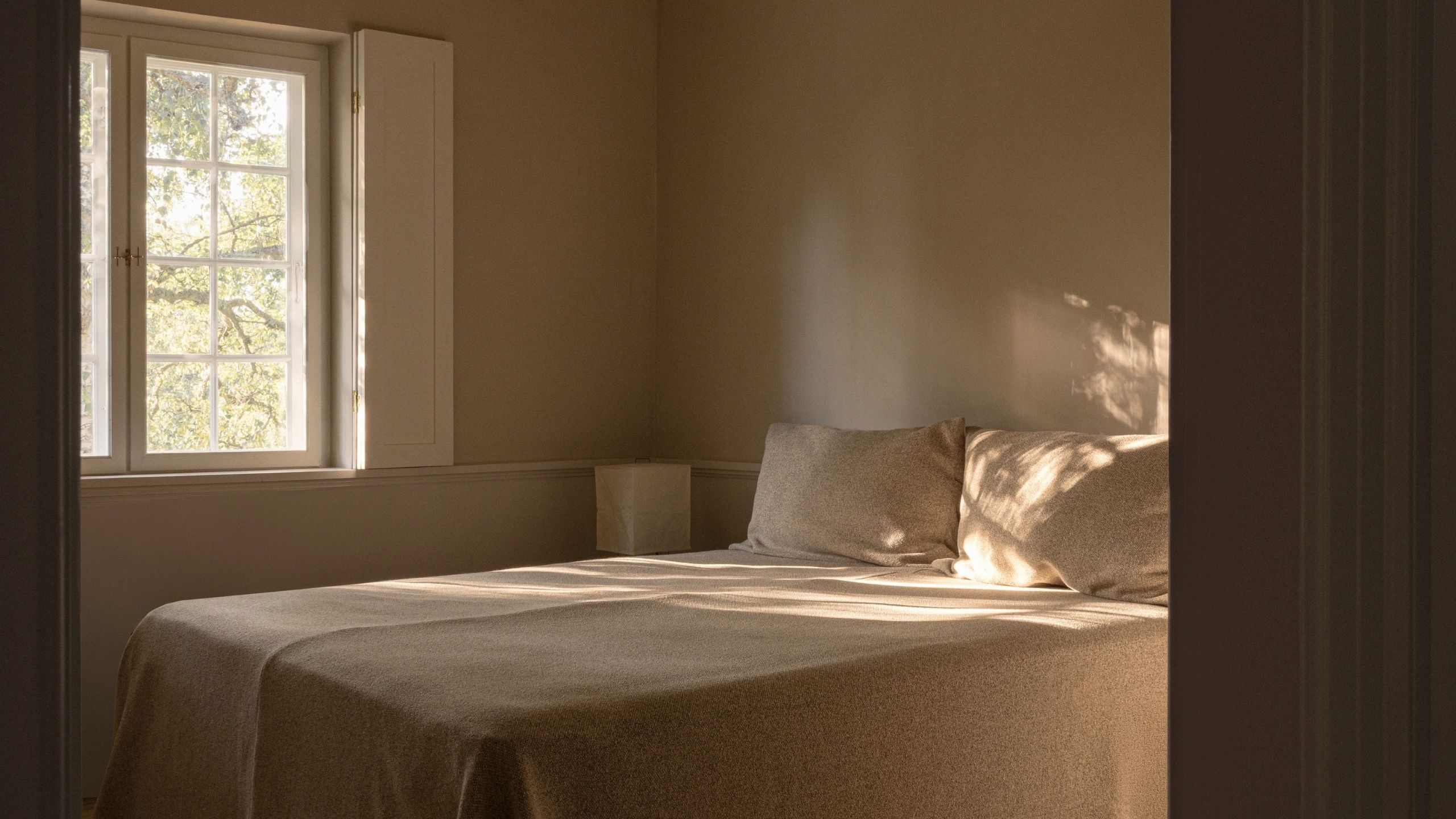 Image of a minimalist, Scandi-style bedroom with a bed that has beige bedding and no headboard.