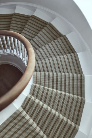 Curved staircase seen from above with white painted stairs and neutral runner