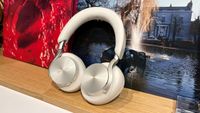A greige pair of Technics EAH-A1000 over-ear headphones standing on a wooden surface in front of record sleeves.