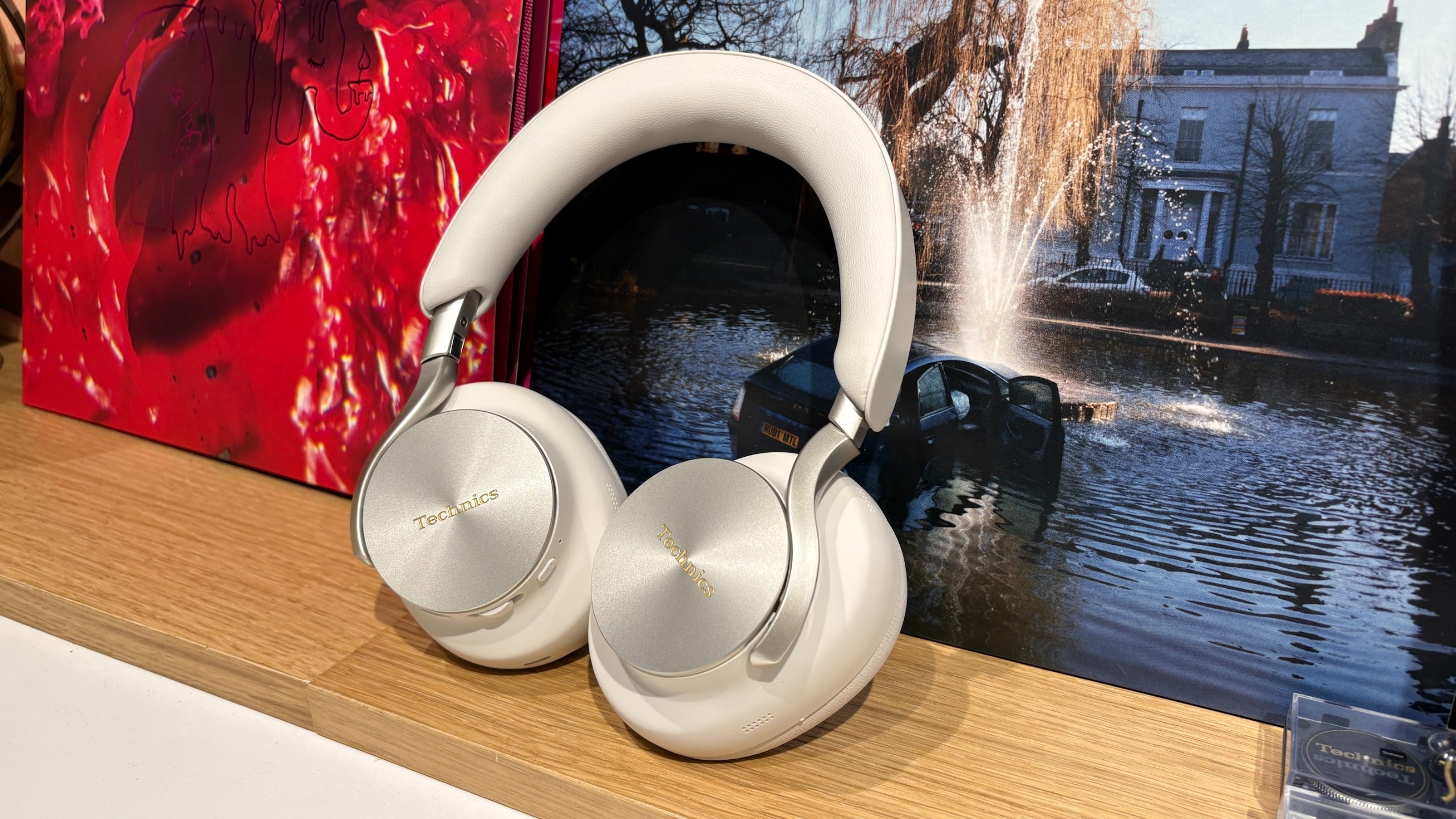 A greige pair of Technics EAH-A1000 over-ear headphones standing on a wooden surface in front of record sleeves.