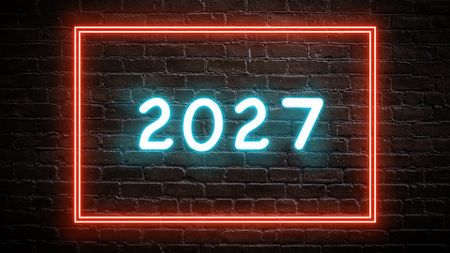 A glowing neon icon showing the year "2027" on a brick wall background.