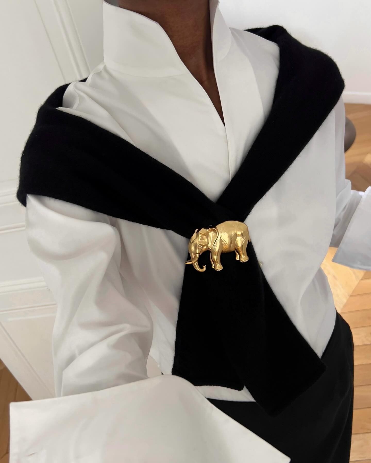 Woman wearing a white button down with a sweater around her shoulders that is clipped to a gold brooch.