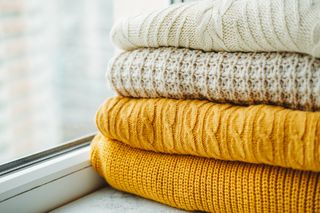 A variety of cream and mustard yellow jumpers folded on top of each other next to a window.