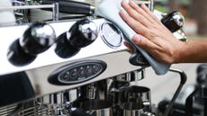 Person's hand wiping front of coffee maker with cloth