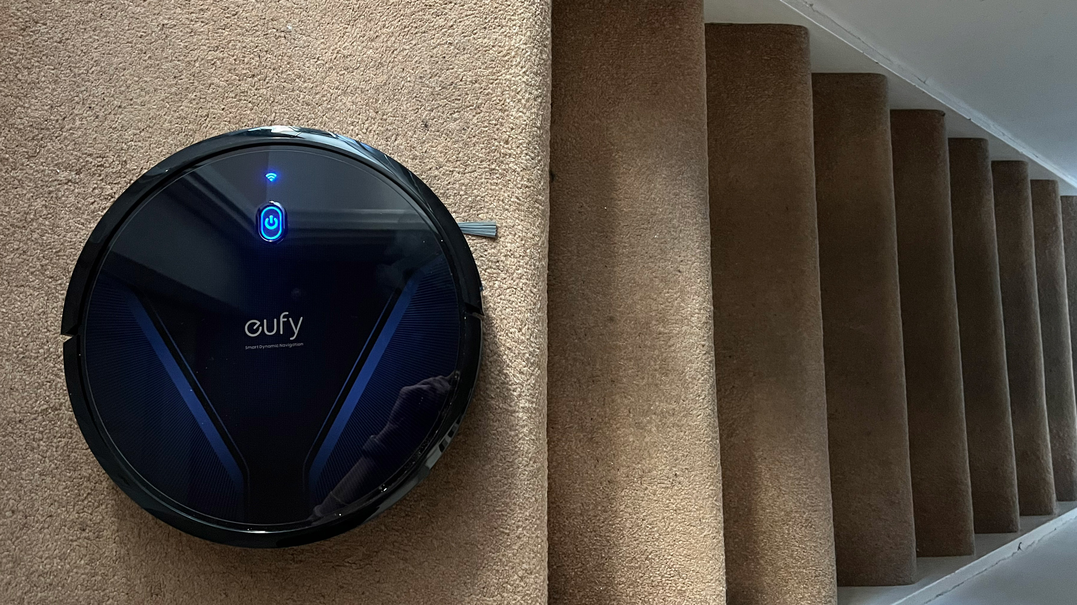 The Eufy RoboVac G20 cleaning carpet next to a set of stairs