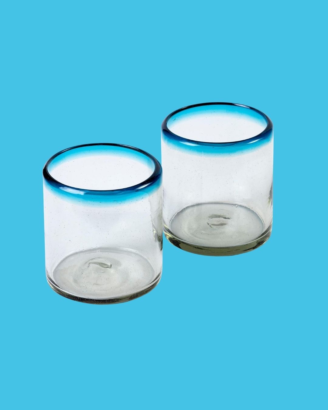 Two transparent tumblers with faded pale blue rim, against a pale blue background.