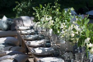 outside dining with table set with plates, glassware, vases full of flowers and foliage, benches with cushions