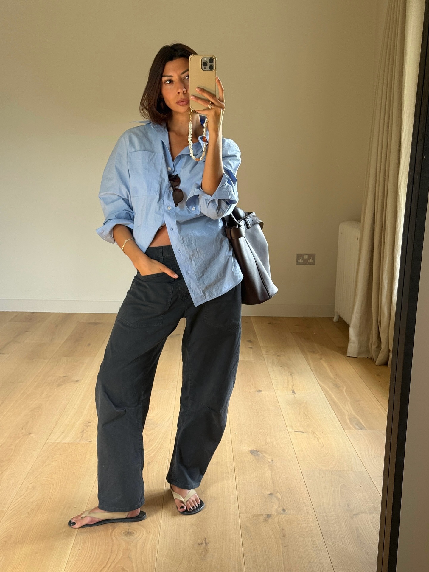 Influencer Marianne Smyth wears barrel leg jeans with a blue button-down, leather tote, and suede sandals.