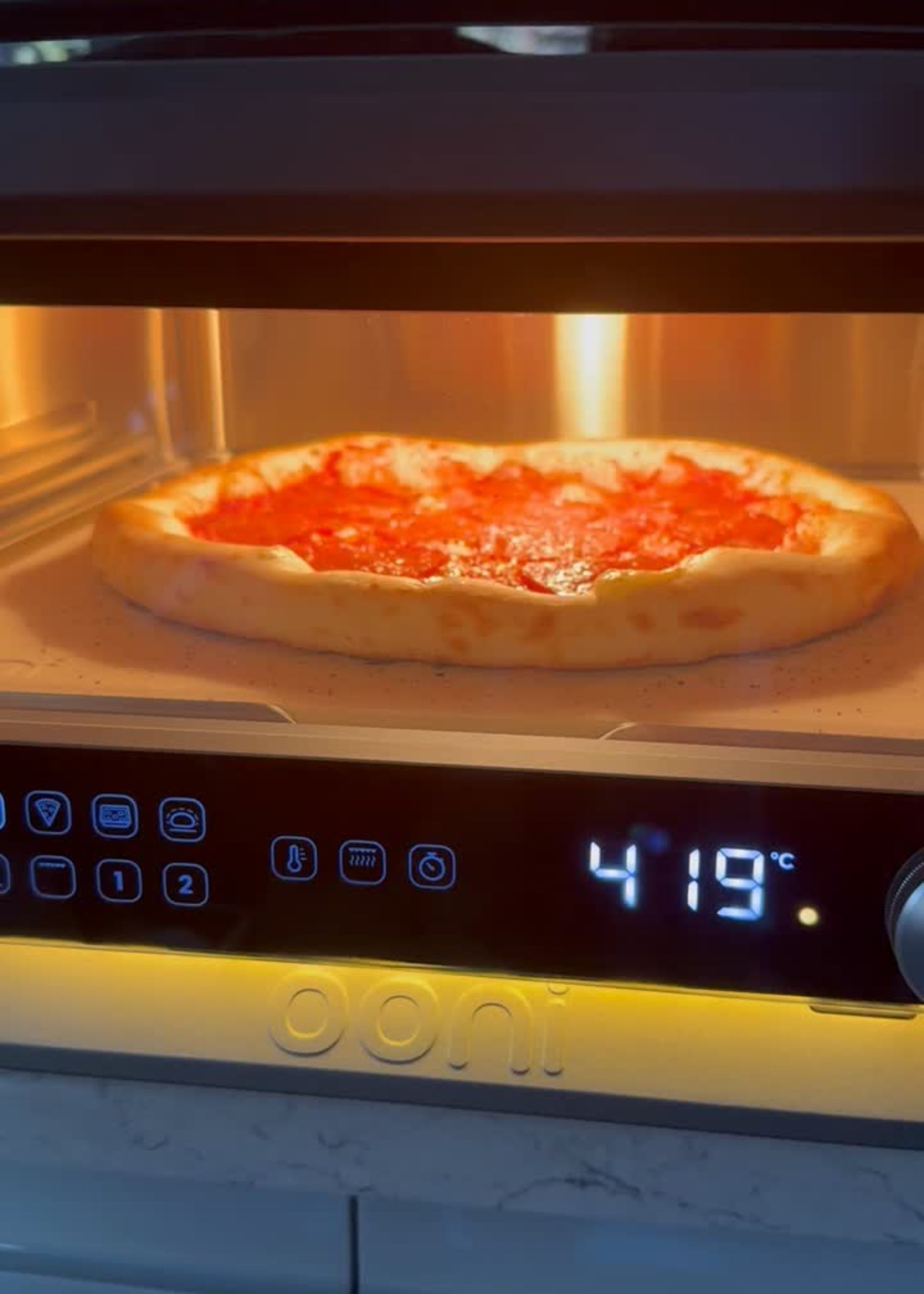 A close up of a pepperoni pizza cooking inside Ooni's volt 2 indoor pizza oven at 419 degrees
