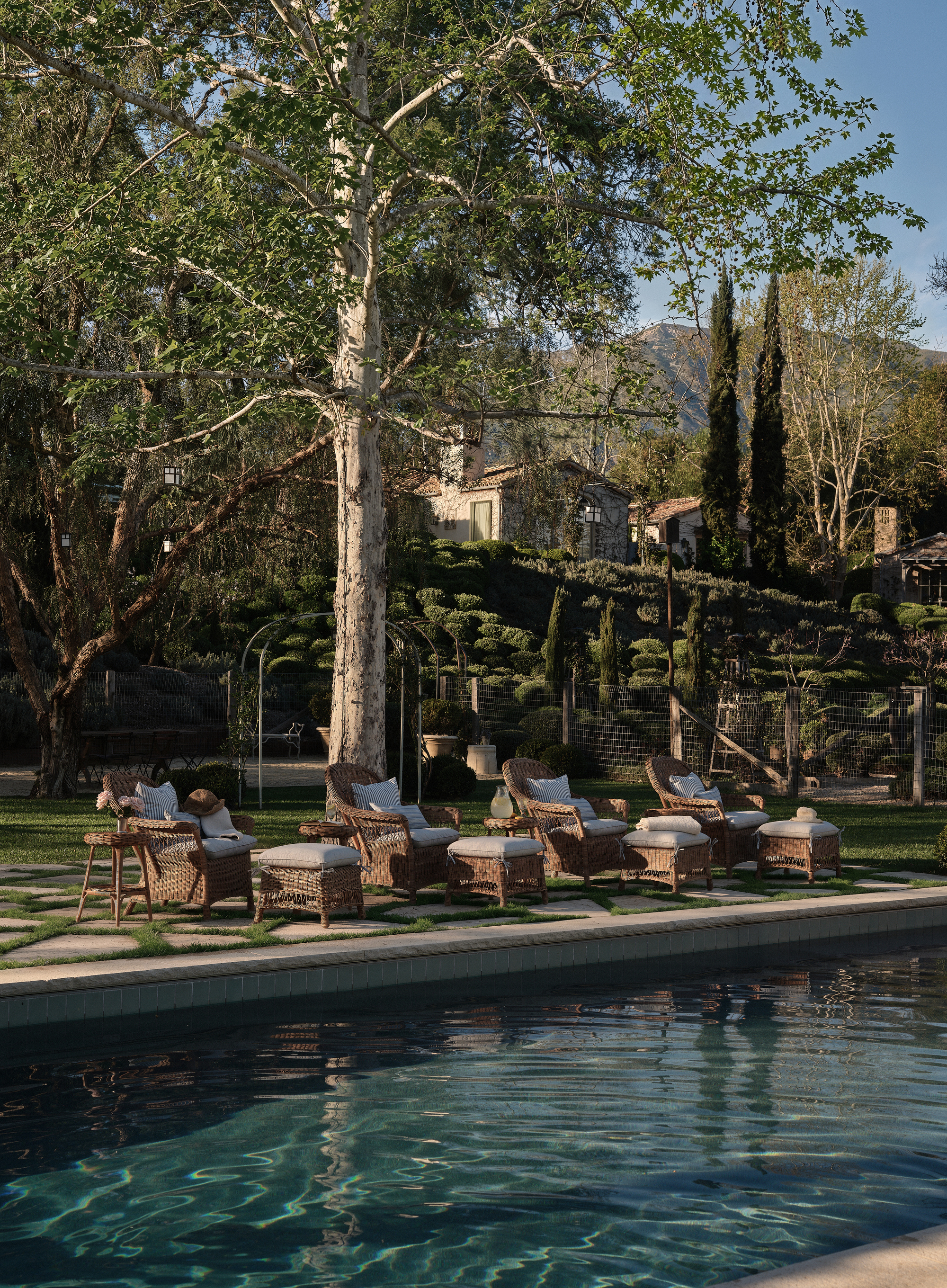 a swimming pool in a large garden with rattan lounge chairs