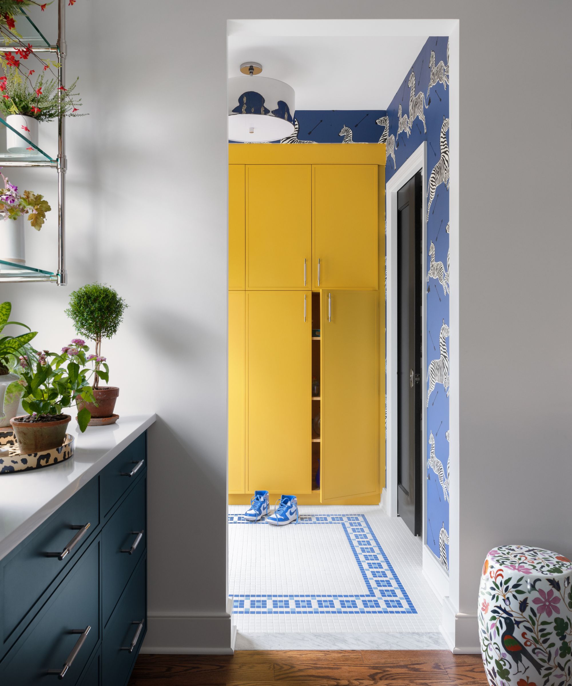 View from a kitchen into a yellow mudroom with mosaic tiles and blue zebra wallpaper
