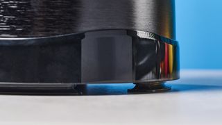 a black nutribullet with a big blending component is photographed in front of a blue backdrop, showing its plastic pitcher jug, silver blades, and tamper