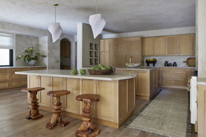 A neutral wooden kitchen with a large bar and organic wooden bar stalls
