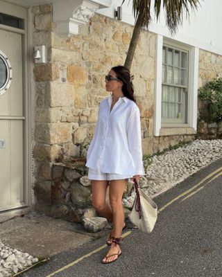 Jessica Skye wearing a long-sleeve linen button down shirt with matching shorts, lace-up sandals, and a beige robe bag.