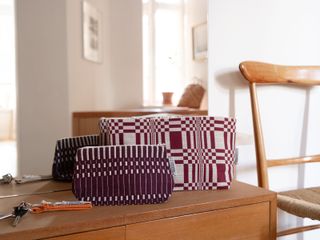 Two toiletry bags in bordeaux and cream sit atop a wooden cabinet standing in front of a mirror in a naturally lit room.