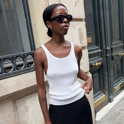 Woman wearing white tank top, black skirt, standing on Paris street.
