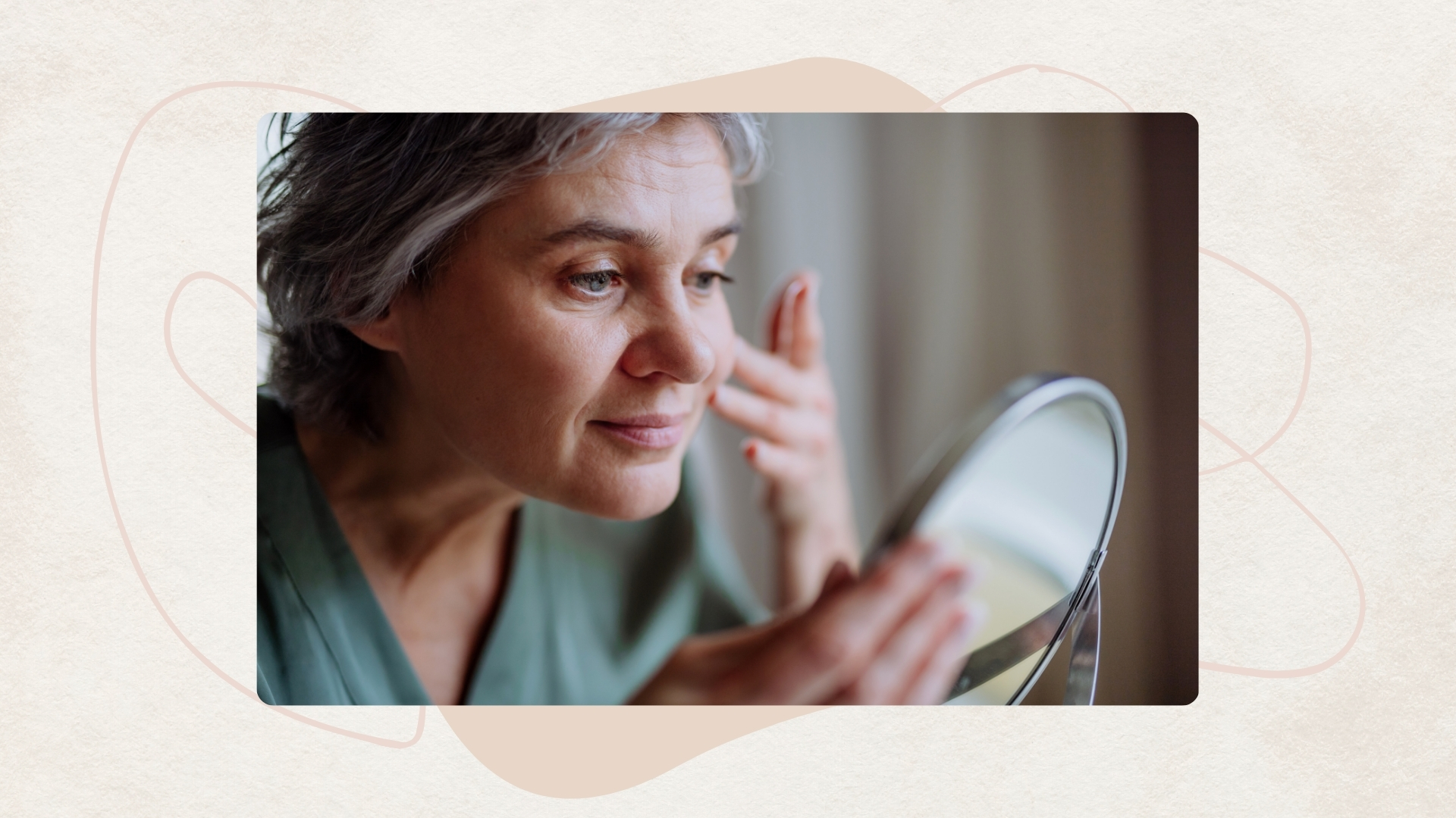 Image of woman with a grey pixie cut looking into a small mirror and touching her face, on a beige background, with beige motif and light pink swirl