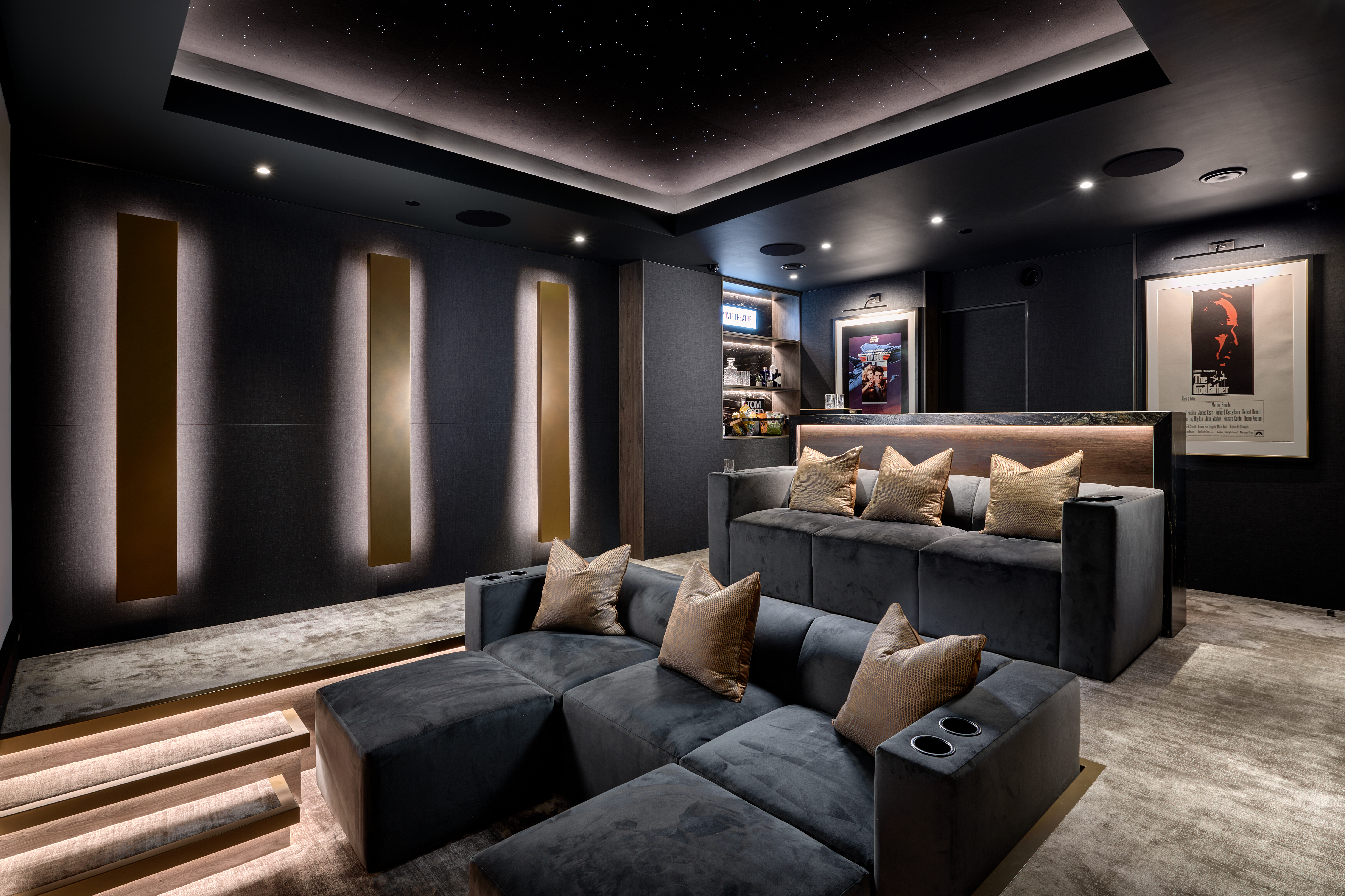 A home theater room showing sofas, a projection screen and warm bronze lighting