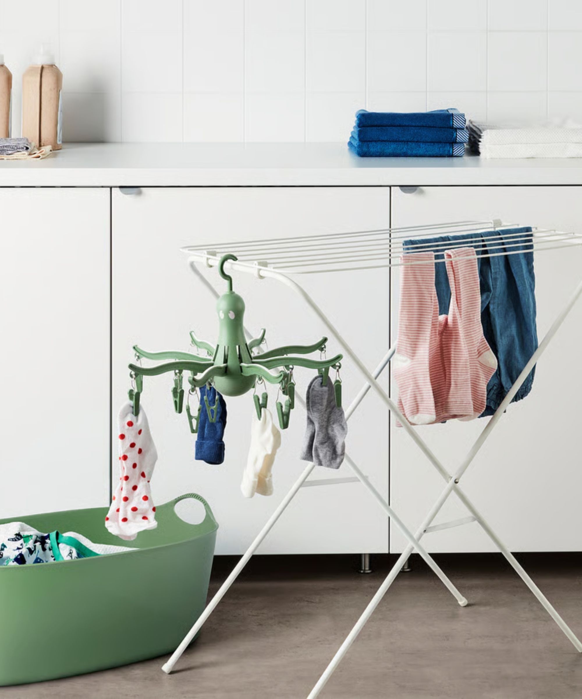 IKEA PRESSA Hanging Dryer pictured hanging beside socks and garments from a white drying rack in a white laundry room with wooden flooring, beside a green plastic laundry basket.