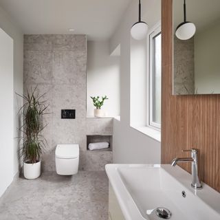 a neutral bathroom with a wall hung toilet and potted house plant