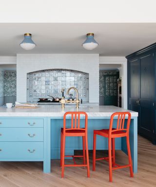 kitchen island color ideas, blue kitchen with sky blue kitchen island, dark blue cabinetry, red bar stools, blue pendants, tiled backsplash, brass taps