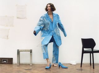 Woman with curly hair stands in a blue plastic suit with blue court heels
