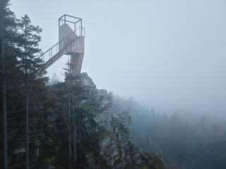Mountain viewpoint structure rising above rocky, tree-covered slopes in low cloud