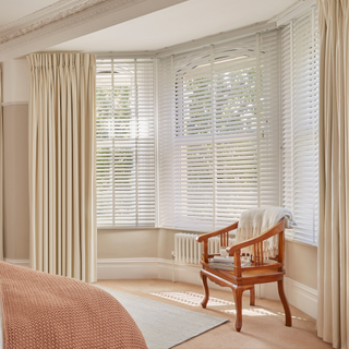 a bedroom bay window dressed with full length curtains and venetian blinds