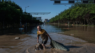 A man pulls bin bags through a flooded street in Beijing
