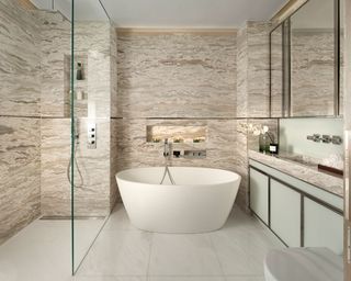 An example of how to design a bathroom showing a large bathroom with marble walls, a white freestanding bath and a walk in shower