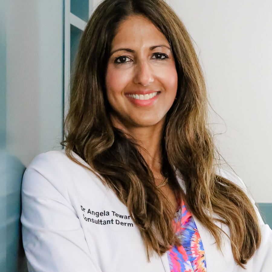 A headshot of a female doctor smiling and wearing a white doctor&#039;s coat