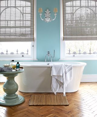 A white freestanding bath on wooden parquet flooring in front of a blue wall