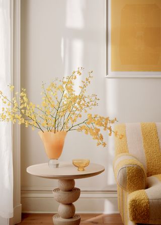 A vase of yellow mimosa stems on a wooden pedestal